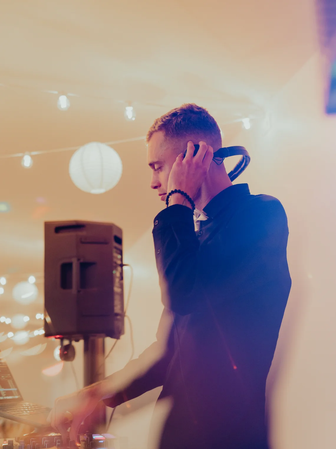 A Pardy DJ cueing the next track behind the booth at a string-lit Fraser Valley wedding reception.